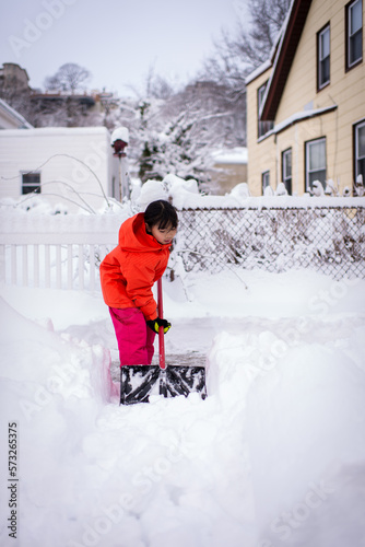 young asian girl shoveling snow after snow blizzard photo