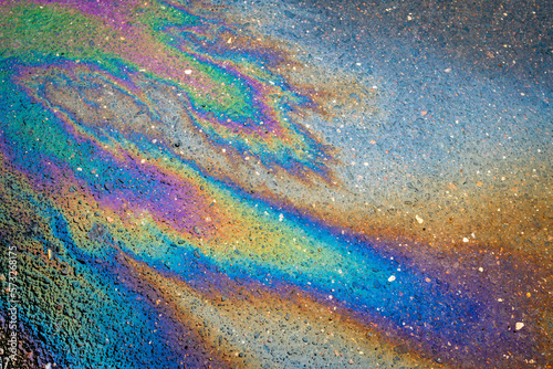 Close-up of an iridescent oil or gasoline spill on a wet asphalt, viewed from above.