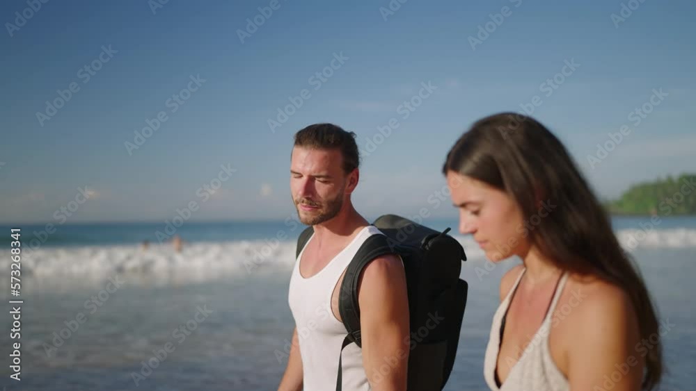 Young biracial happy couple holding hands walking and talking on the beach together enjoying summer closeup. Cheerful boyfriend and girlfriend relaxing and walking by the seaside at sunrise.