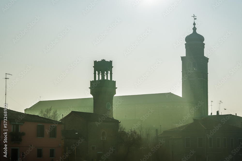 Murano, Italy evening view of Campanile silhouettes with sun above Saint Pietro Martire church & Torre dell Orologio.