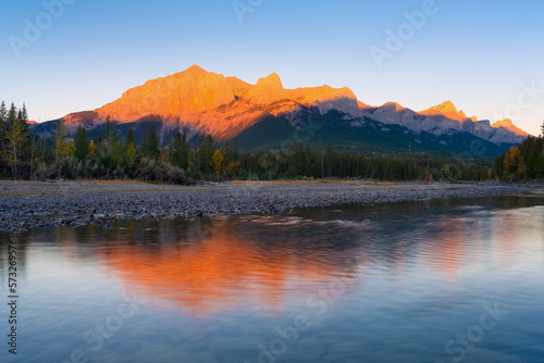 Landscape during sunrise. Autumn trees on the river bank. Mountains and forest. Reflections on the surface of the river. Vivid colours during dawn. Natural landscape.
