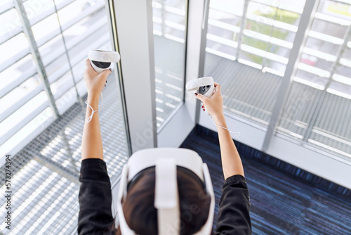 Overhead picture of young woman using VR glasses with controllers in modern office