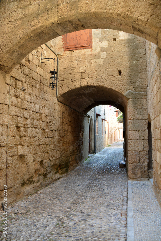 Obraz premium ancient medieval street with narrow entrance, arch and pebbled pathway
