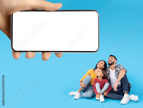 Happy Arabic Family Looking At Big Blank Smartphone In Giant Female Hand