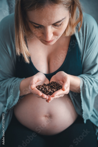 Young blonde pregnant woman, close up, looking and holding coffee beans with her hands
