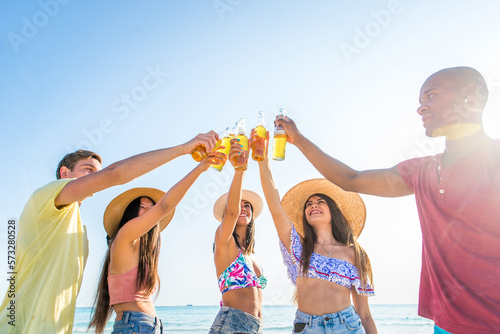 Happy multiethnic group of friends having summer vacation and having fun on the beach - Young people bonding together at the sea