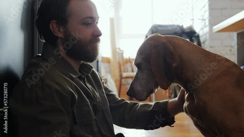 The caring owner and his hunting dog pointer are sitting on the kitchen floor. The owner is a man stroking his dog at home. High quality 4k footage