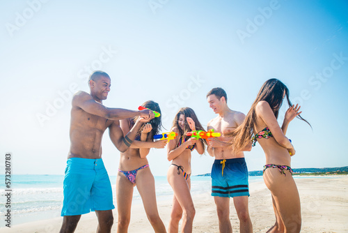 Happy multiethnic group of friends having summer vacation and having fun on the beach - Young people bonding together at the sea