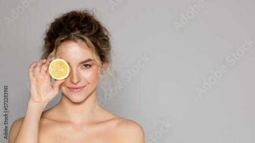 Beautiful woman holding lemon half and looking at camera, lady using vitamin c fruit acids for beauty care, copy space