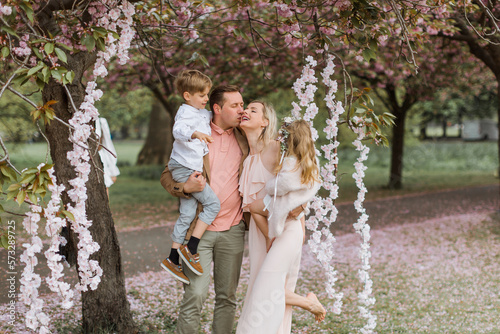 Spring. Happy couple in sakura park. Happy family in spring garden. Tourist family walk in park. Mother, father and two kids at blooming sakura park. Spring sakura bloom. Family walk in sakura park. © Myroslava