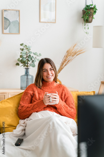 Happy woman with cup of hot drink watching tv