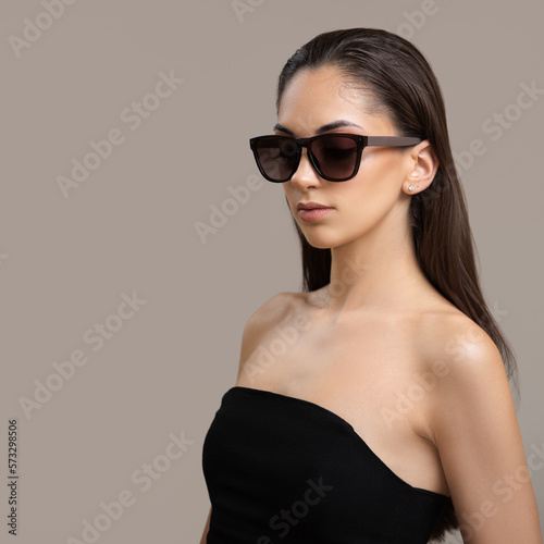 Young stylish woman in black sunglasses on a gray background.