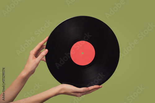 Women's hands hold a vinyl disc. Green background.