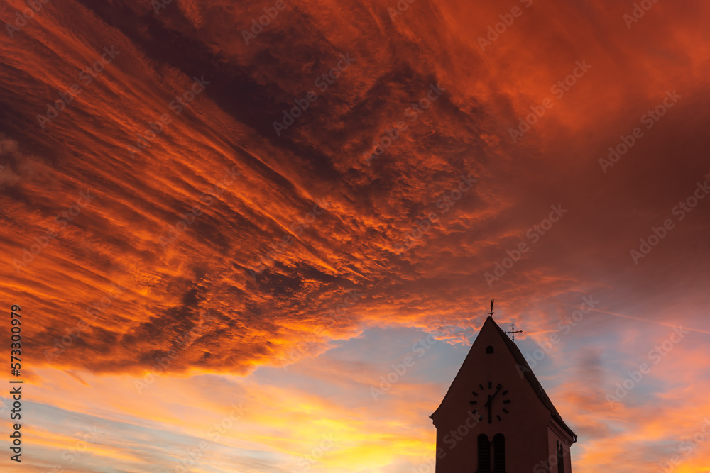 Silhouette of a church steeple under a cloudy orange sky at sunset. Silhouette of a church steeple under a cloudy orange sky at sunset.