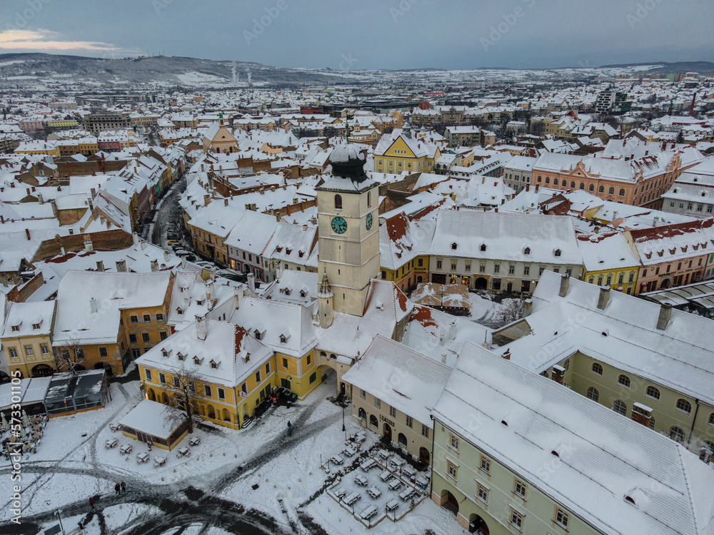 Birds eye view over historic city center of Sibiu, Romania at sunset. Drone photography of cityscape  from above containing the small square and the tower of the city hall. - obrazy, fototapety, plakaty 