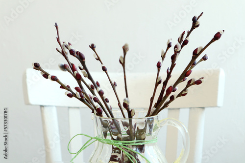  Spring mood: a bouquet of flowering willow branches in a glass vase against the background of a white chair, space for text
