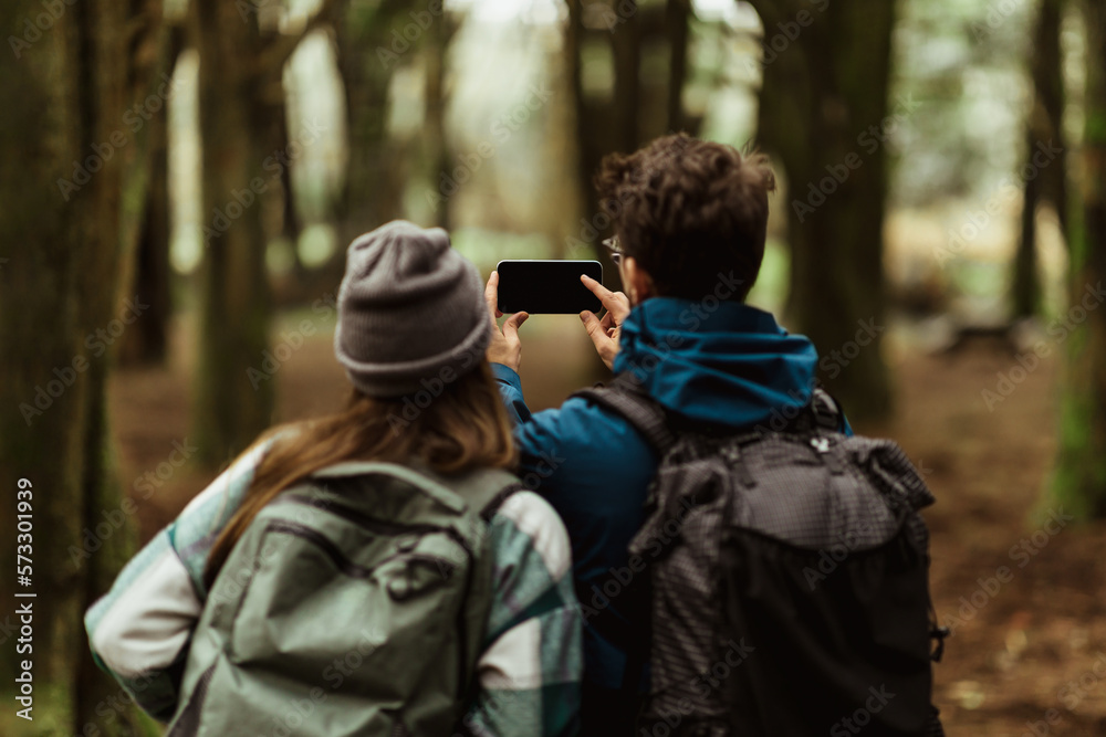 Millennial caucasian woman and guy in jacket and backpack take selfie on phone with blank screen