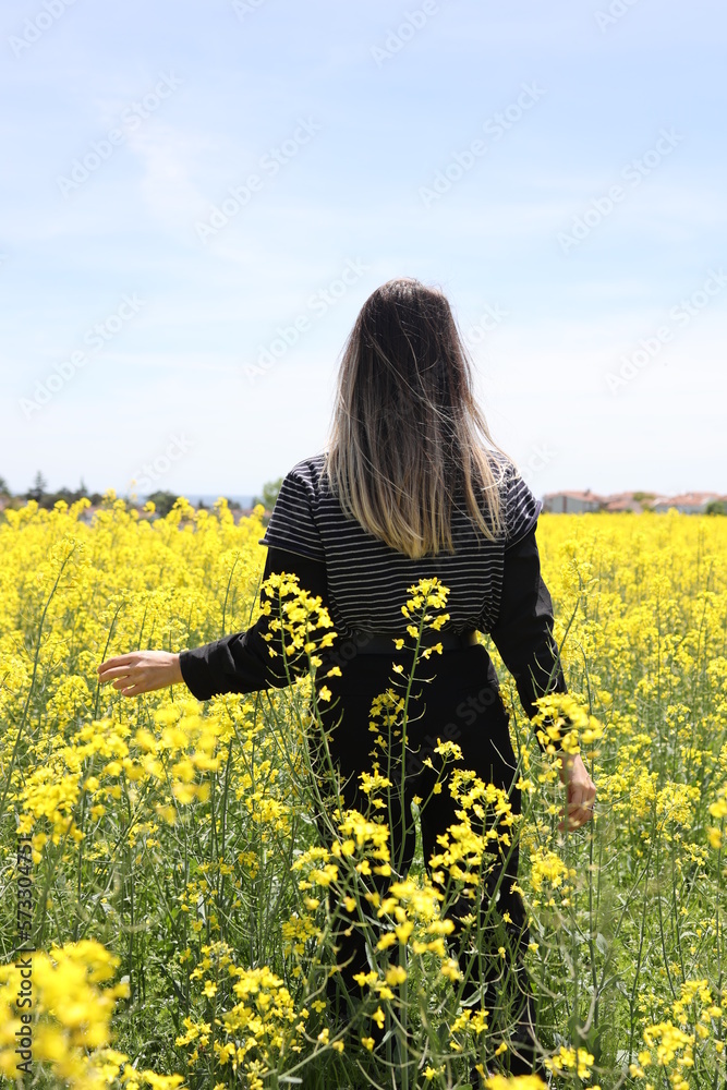 Back View of a Young Woman Standing on the Flower Field. Canola Field. Back View of a Young Woman Standing on the Flower Field. Canola Field.