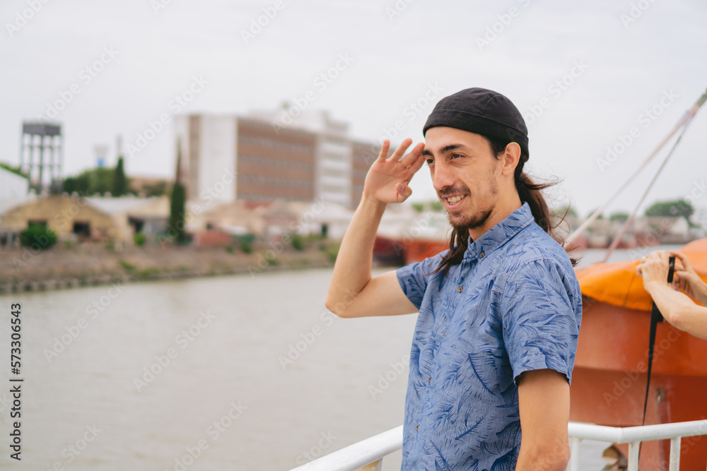 Young latin man in civilian clothes in a harbor doing military salute. Copy space.