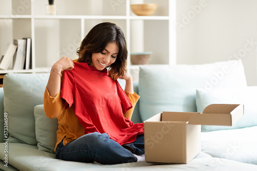 Smiling Young Middle Eastern Female Unpaking Box With New Clothes At Home photo