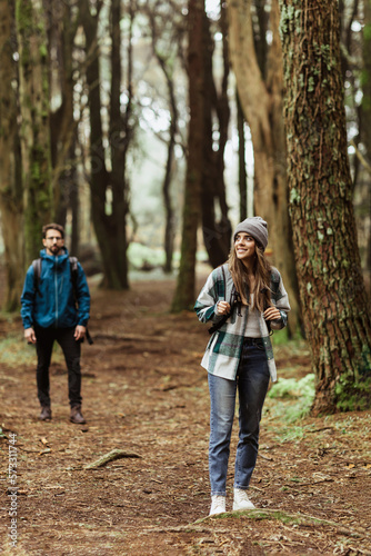 Happy millennial caucasian man and woman in jackets and backpacks travel in cold forest, enjoy adventure © Prostock-studio
