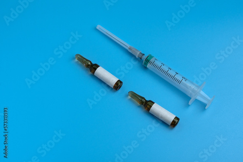 A medical syringe and two ampoules are isolated on blue background. Ampoules for injections. Healthcare, medicine, and vaccination concept. 