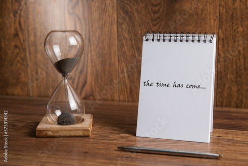 Glass hourglass and notepad with the inscription the time has come