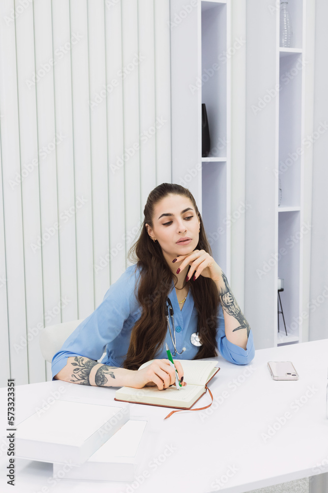 This photo shows a cosmetic dermatologist taking notes at her desk, surrounded by plants, books, and accessories. Her blue coat and professional focus convey a sense of clinical precision. This photo shows a cosmetic dermatologist taking notes at her desk, surrounded by plants, books, and accessories. Her blue coat and professional focus convey a sense of clinical precision.