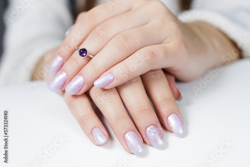 The hands of a young woman. The nails are covered with pearl gel polish with glitter