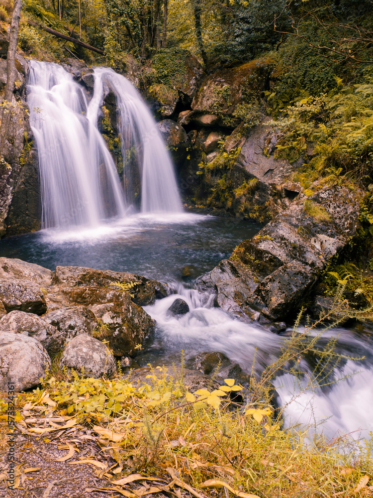 Fototapeta premium Vista de la Cascada de Narahío, con agua cayendo formando un lago azul rodeado de vegetación, en La Coruña, Galicia, verano de 2021.