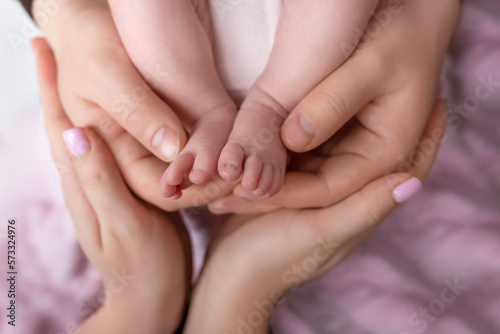Little feet of a newborn baby girl in the hands of father and mother on a pink background. baby feet in parental hands