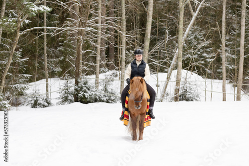 Icelandic horse and female rider riding on snowy field. Rider has black helmet.