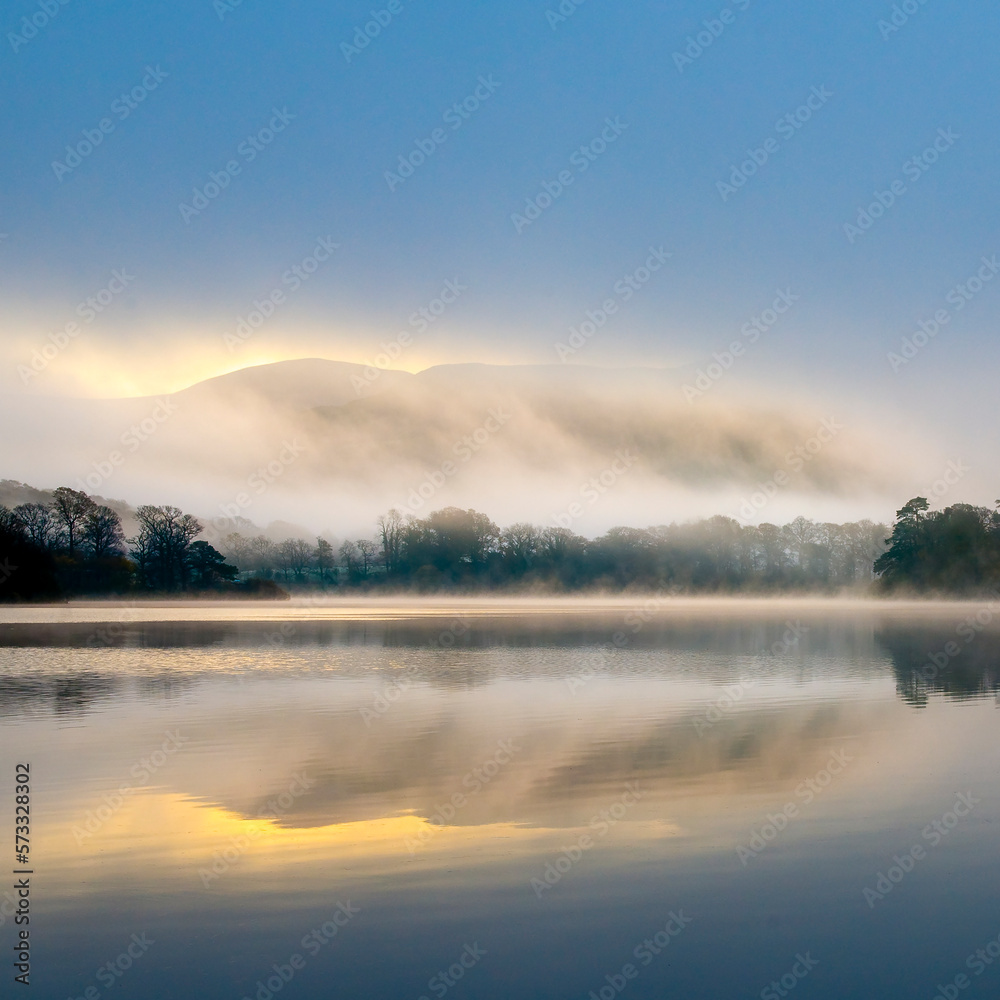 Misty fells across a still lake at dawn