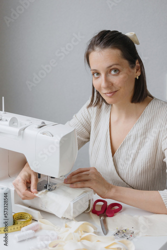 woman on sewing machine creates clothes and suits, female cutter fashion designer couturier makes collection of dresses. home workshop or atelier of individual tailoring. handmade work area