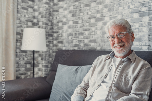 Portrait of happy mature 80s man sit on couch at home look at camera posing relaxing on weekend, smiling positive senior 70s grandfather rest on sofa at home or retirement house, show optimism.