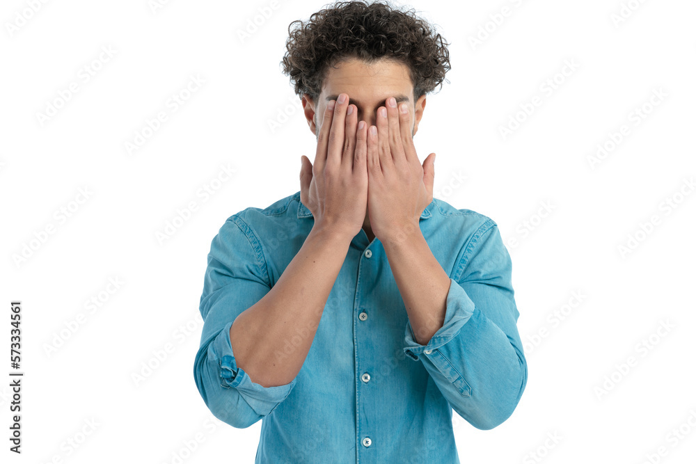 timid young man with curly hair covering face with palms timid young man with curly hair covering face with palms