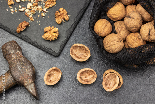 Walnuts in a reusable bag. Hammer, nut shells on the table and nut kernels on stone board.