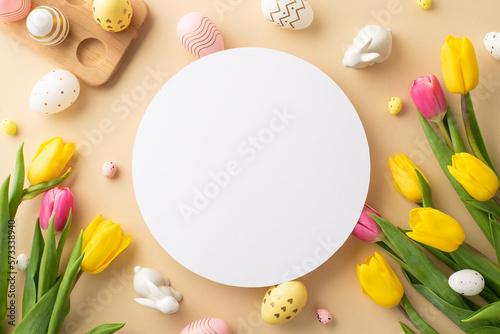 Easter concept. Top view photo of white circle easter eggs in wooden holder ceramic bunnies yellow and pink tulips on isolated pastel beige background with copyspace