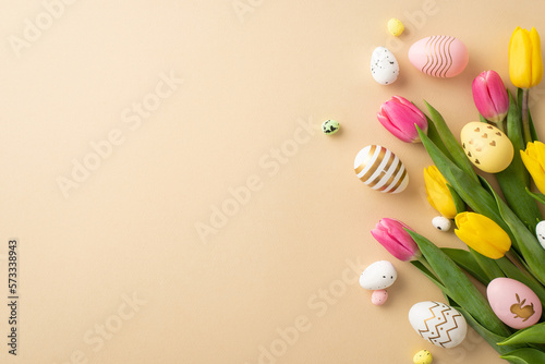 Easter celebration concept. Top view photo of colorful easter eggs yellow and pink tulips on isolated pastel beige background with copyspace #573338943