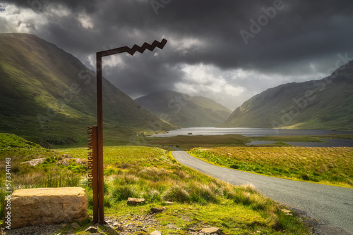Doolough Valley sign with lakes, Glenummera and Glencullin mountain ranges in background, dark dramatic sky, County Mayo, Ireland photo