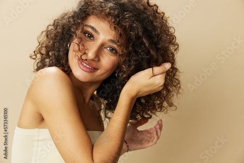 Woman applies cream and balm to her curly hair, the concept of protection and care, a healthy look, a smile with teeth on a beige background