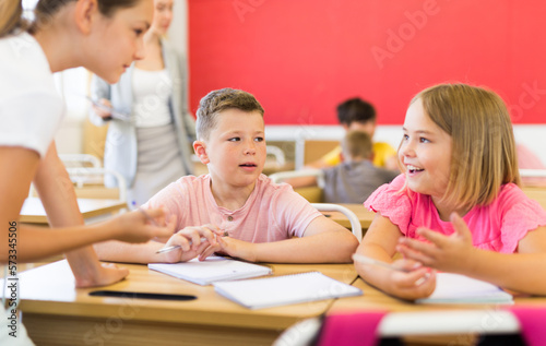 Preteen schoolchilds working in groups at lesson in primary school with teacher on background