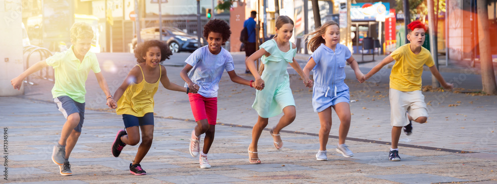 Obraz premium Group of smiling kids holding each other hands while running through city streets together.
