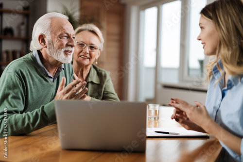 Happy mature couple and their counselor communicating while using laptop on a meeting at home © Goran