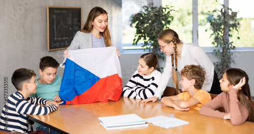 Teacher holds the flag of Czech in her hands and tells the students about this country