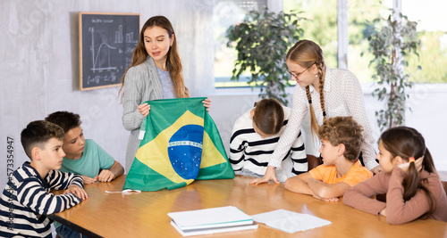 Teacher holds the flag of Brazil in her hands and tells the students about this country