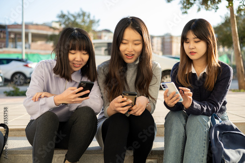 Group of girls with Asian features sitting on the steps of a street each with a mobile phone. Losing communication. people using their phones and texting. photo
