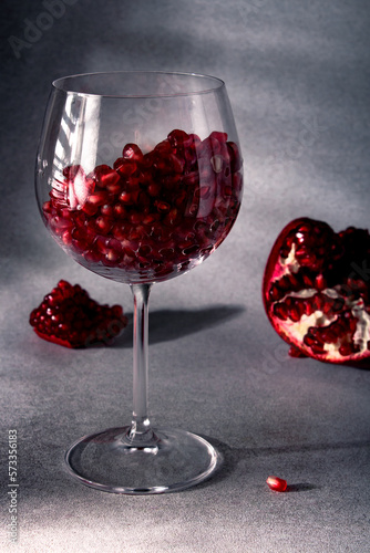 Pomegranate seeds in a wine glass and ripe pomegranate pieces nearby. Pomegranate wine. The concept of romance. Healthy food concept. Seasonal winter fruits. Source of iron.