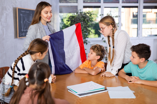 Geography lesson in school class - teacher talks about France, holding a flag in his hands