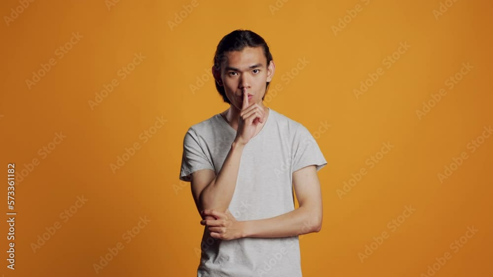 Male model doing mute silent gesture in studio, doing hush sign to keep secret and confidential news. Private adult keeping privacy and secrecy on camera, being careful with information. Male model doing mute silent gesture in studio, doing hush sign to keep secret and confidential news. Private adult keeping privacy and secrecy on camera, being careful with information.
